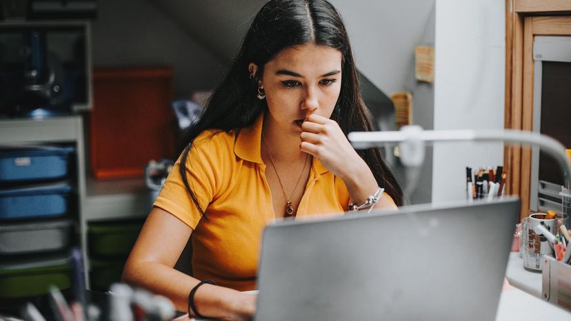 Young woman in an orange shirt working on a laptop in a dorm room