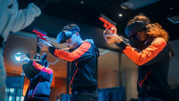 Three people in matching jackets aiming toy guns and wearing VR sets