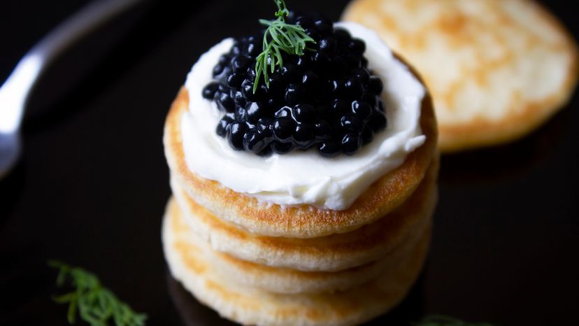 Black caviar blinis with cream cheese and fresh dill stacked.