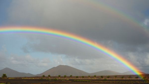 A double rainbow stretches across a hilly landscape