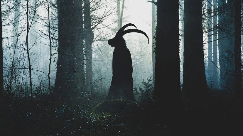 Silhouette of a horned being in a robe standing in a dark forest