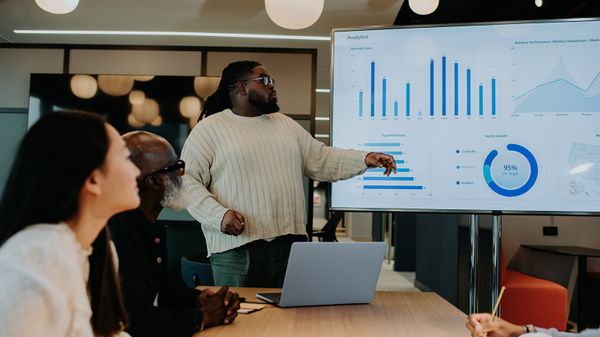 A man presents graph data on a large screen to his colleagues in an office