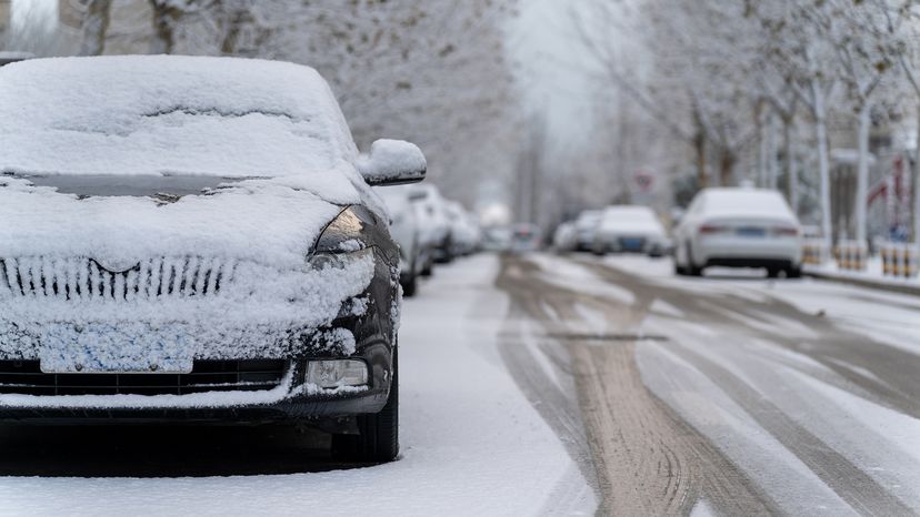 Wide view of heavy snow covered street with lots of parked, snow-covered cars.