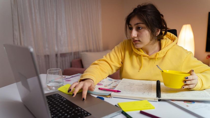 Student in yellow hoodie using laptop with open books