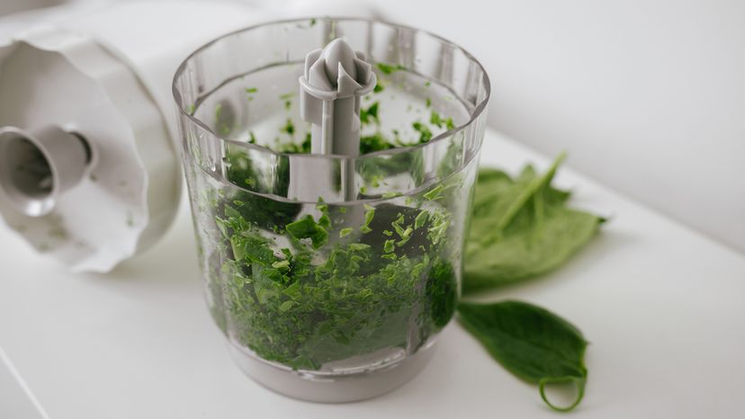 Blender bowl of green spinach on white table.