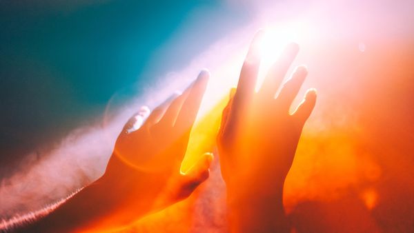 Two hands reaching for a distant light with a heavy saturation filter