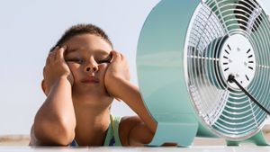 Overheated child sitting in front of electric fan trying to cool down