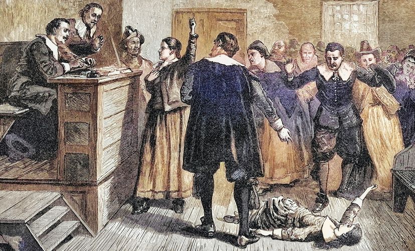 Engraved illustration of a Salem witchcraft trial. A man points at a girl writhing on the floor.
