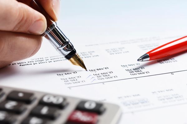 A hand holding a pen, marking up an accounting ledger.