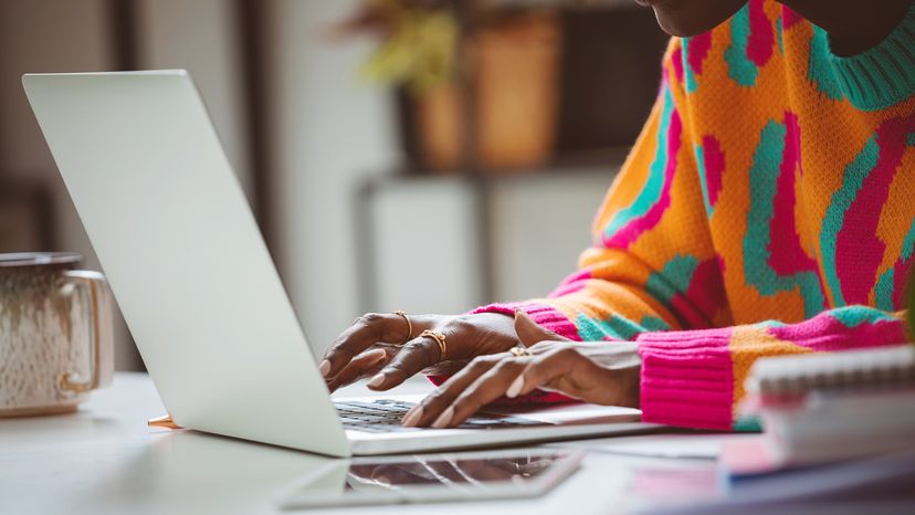 Woman wearing colorful sweater sitting at the desk and typing on a laptop