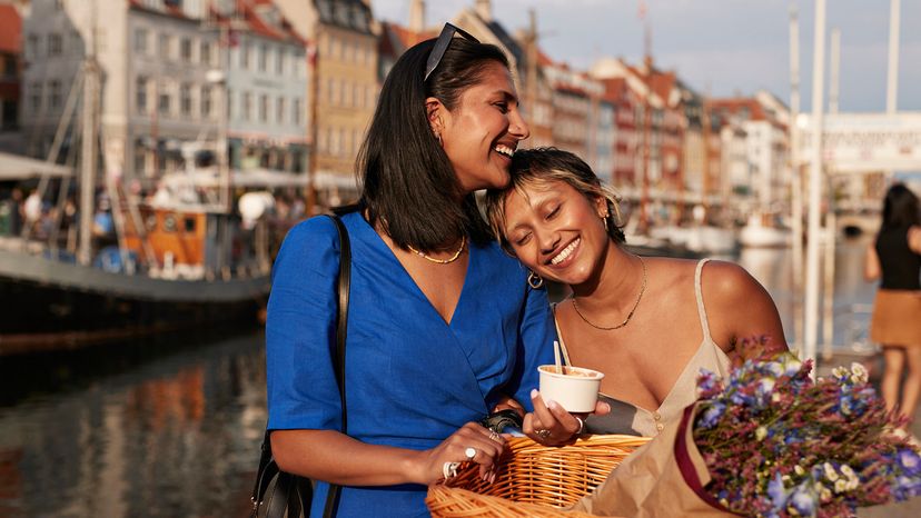 Smiling young woman with bicycle leaning on another woman near river