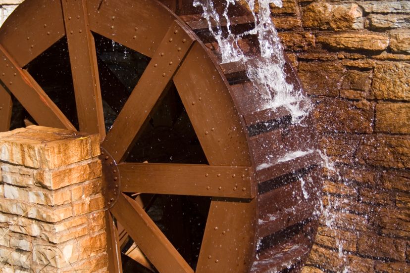 A wooden water wheel turning and generating power outside a stone wall