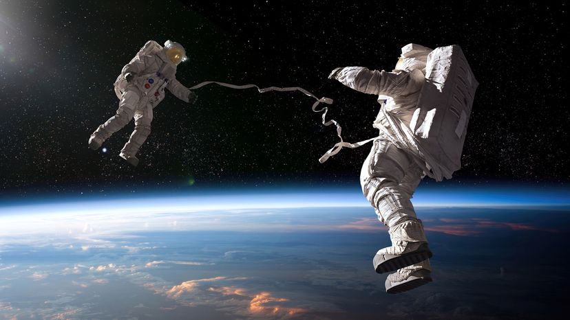 Two astronauts in full spacesuits floating above Earth