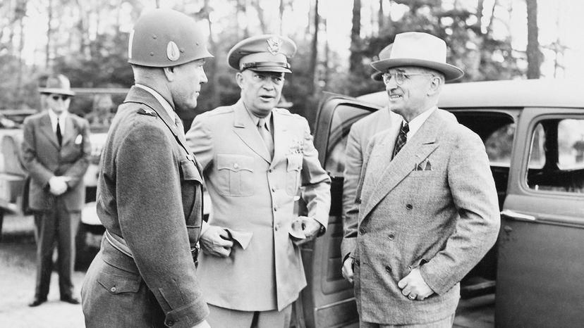 Black and white photo a man in a suit speaking with two men in military uniforms