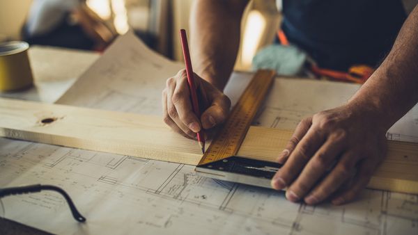 Close up of unrecognizable carpenter making measurements and drawing on a plank.