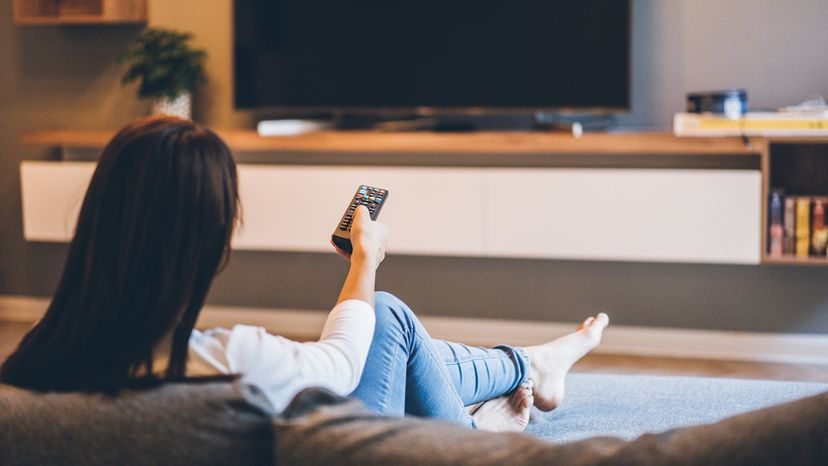 Woman watching TV, sitting on the sofa at home, back view