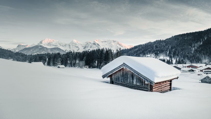 cabin buried in thick layer of snow with woods and mountains in background