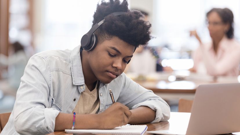 Student in a library, wearing headphones and studying