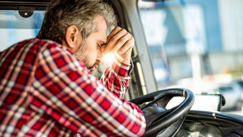 Distraught truck driver leaning on a steering wheel and having a headache.