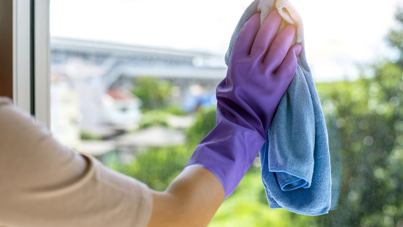 gloved hand using a microfiber towel to clean a window