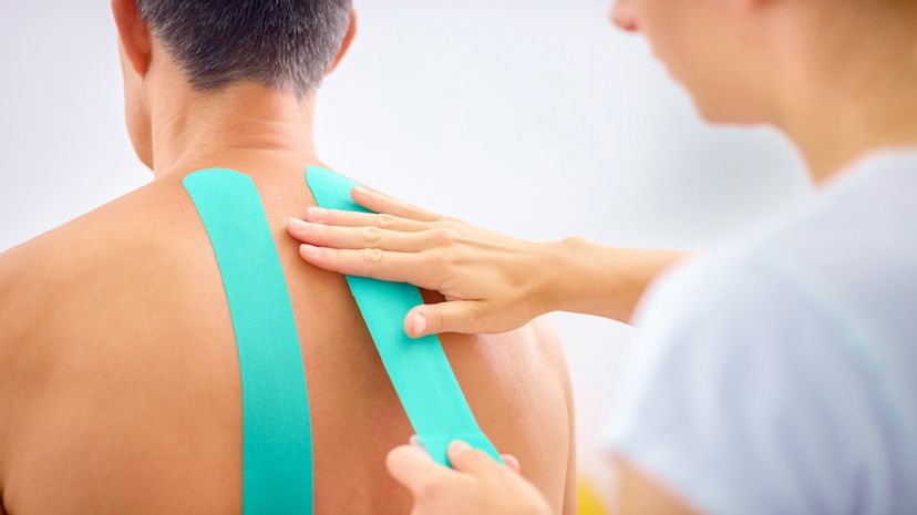 Close-up of womans hands applying kinesio tape on mature mans back during treatment.