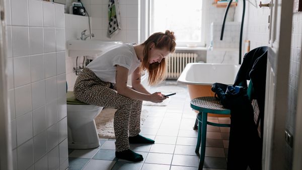 A girl sitting on the toilet in her bathroom and using her smartphone
