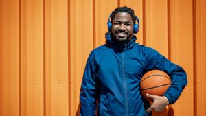 man in blue jacket holding a basketball in front of orange background