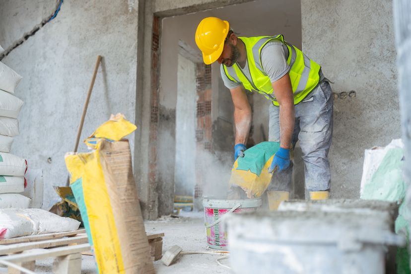 一名建筑工人混合水泥制造混凝土在一个建筑工地。”width=