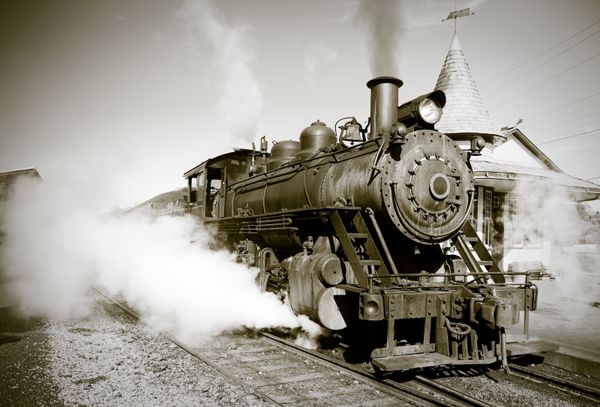 A sepia-toned photo of a vintage steam locomotive beginning its journey from the station