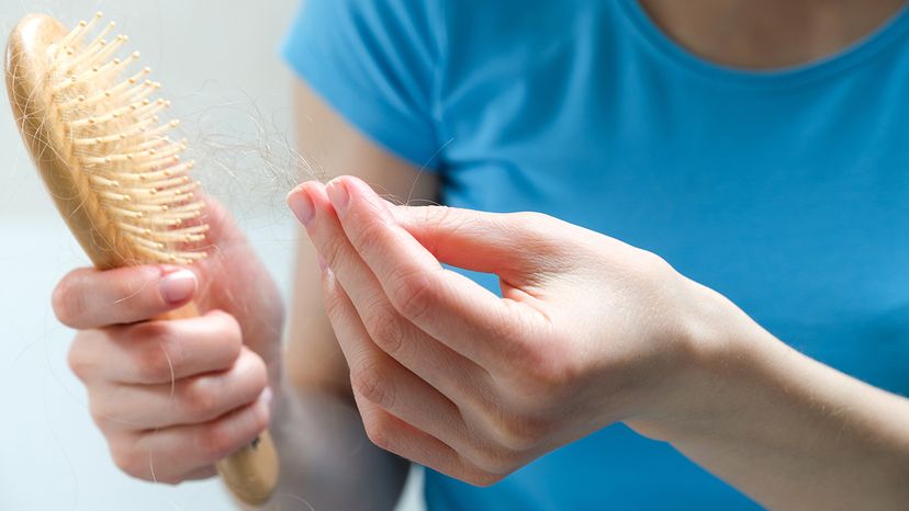 Woman cleans pulls hair out of a wooden hairbrush