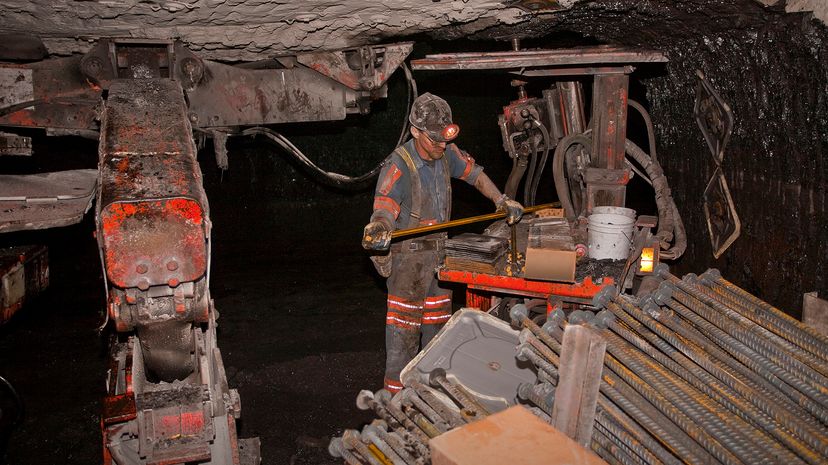 Man using heavy machinery in a dark, grimy coal mine