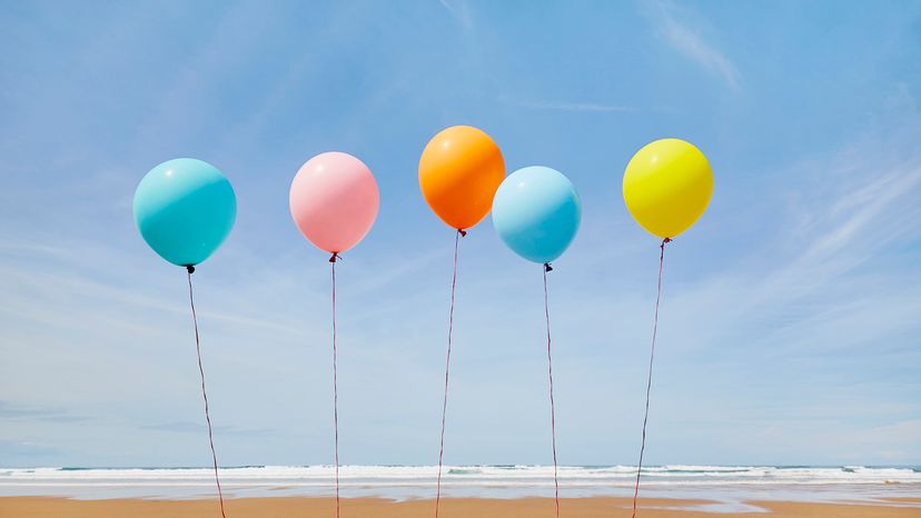 Five colorful balloons in a row against blue sky at the beach