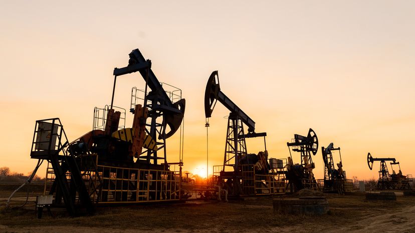 The silhouette of oil pumps on a beautiful sunset sky with sun setting in between them.