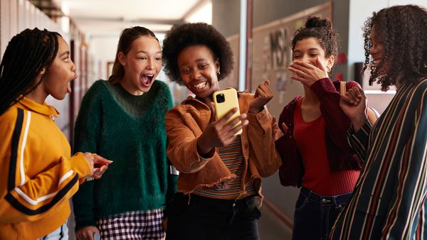 Girl sharing smart phone with shocked friends in school hallway