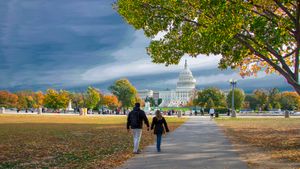 Two people walk toward the capitol building on a fall day
