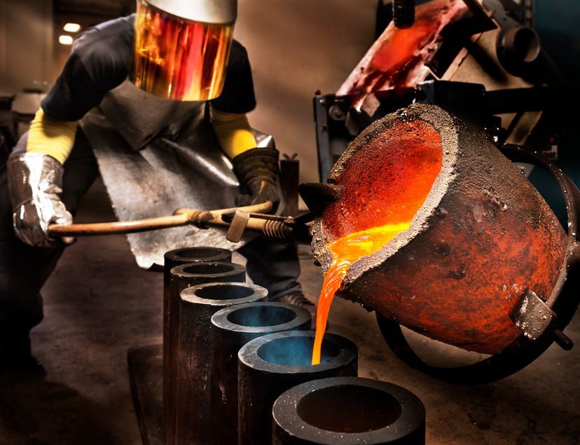 A worker wears a specially shielded visor while pouring molten metal into a crucible.