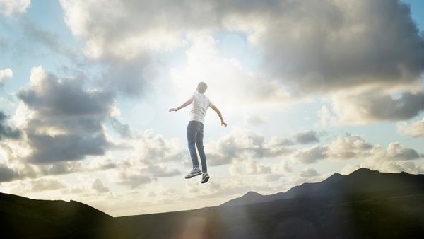 Man levitating above a mountain silhouette, looking at a cloudy sky