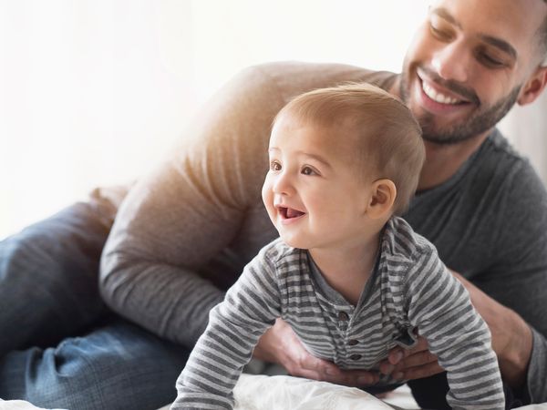 Smiling father playing with baby son on bed