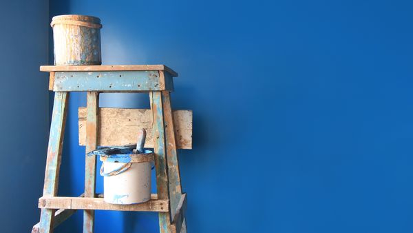 Paint cans on a dirty ladder in front of a wall freshly painted blue