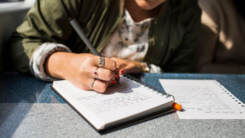 A person wearing three rings uses a pen to write in a journal