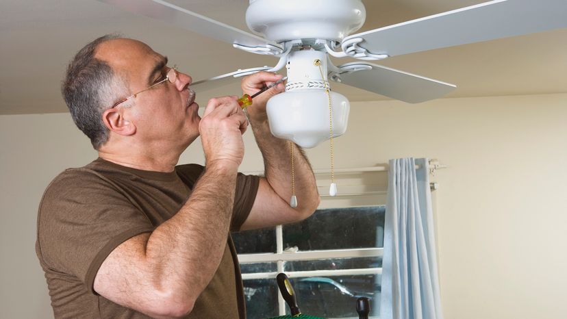 Man with a screwdriver working on a white ceiling fan