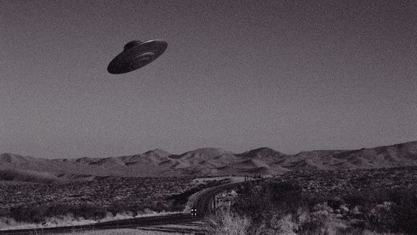 Grainy, black and white photo of a flying saucer over a mostly empty desert highway