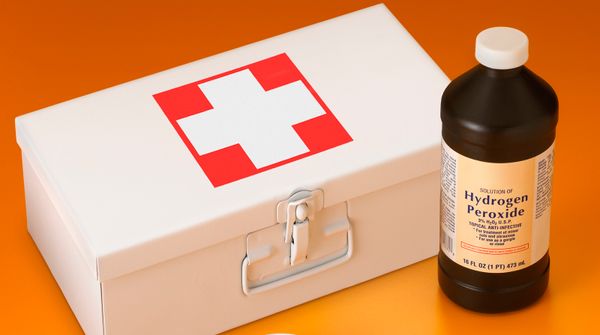 a bottle of hydrogen peroxide beside a closed first aid kit