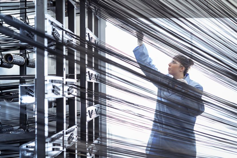 A woman inspects metal threads on a large power loom.