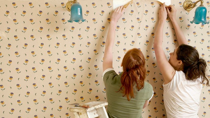 two women peeling wallpaper off a wall