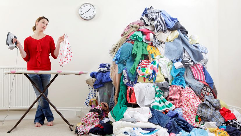 Woman with iron and ironing board standing beside giant pile of laundry