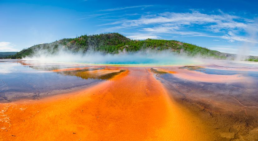 A wide-angle view of Grand Prismatic Spring with clouds overhead in Yellowstone National Park.