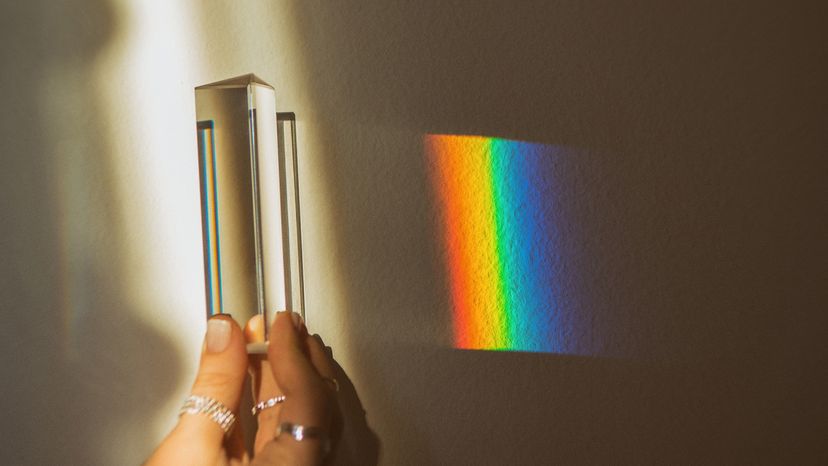 Human hand holding prism while making rainbow on wall