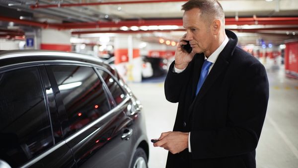 Man talking on a cell phone and holding a key fob beside a black car in a parking structure