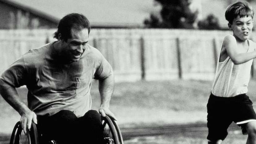Black and white photo of a man in a wheelchair racing his son around a track